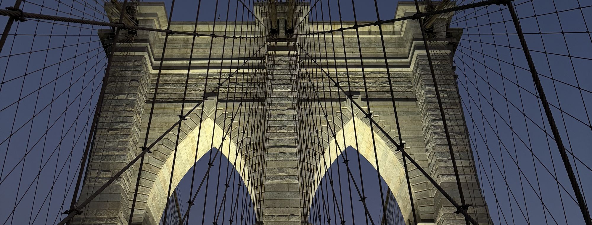 The Brooklyn Bridge at dusk, its stone towers and cables against a deep blue sky