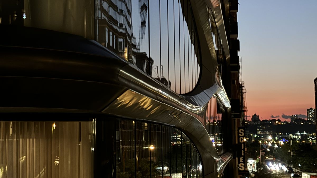 A curving glass building at dusk, with the sunset over the river behind it